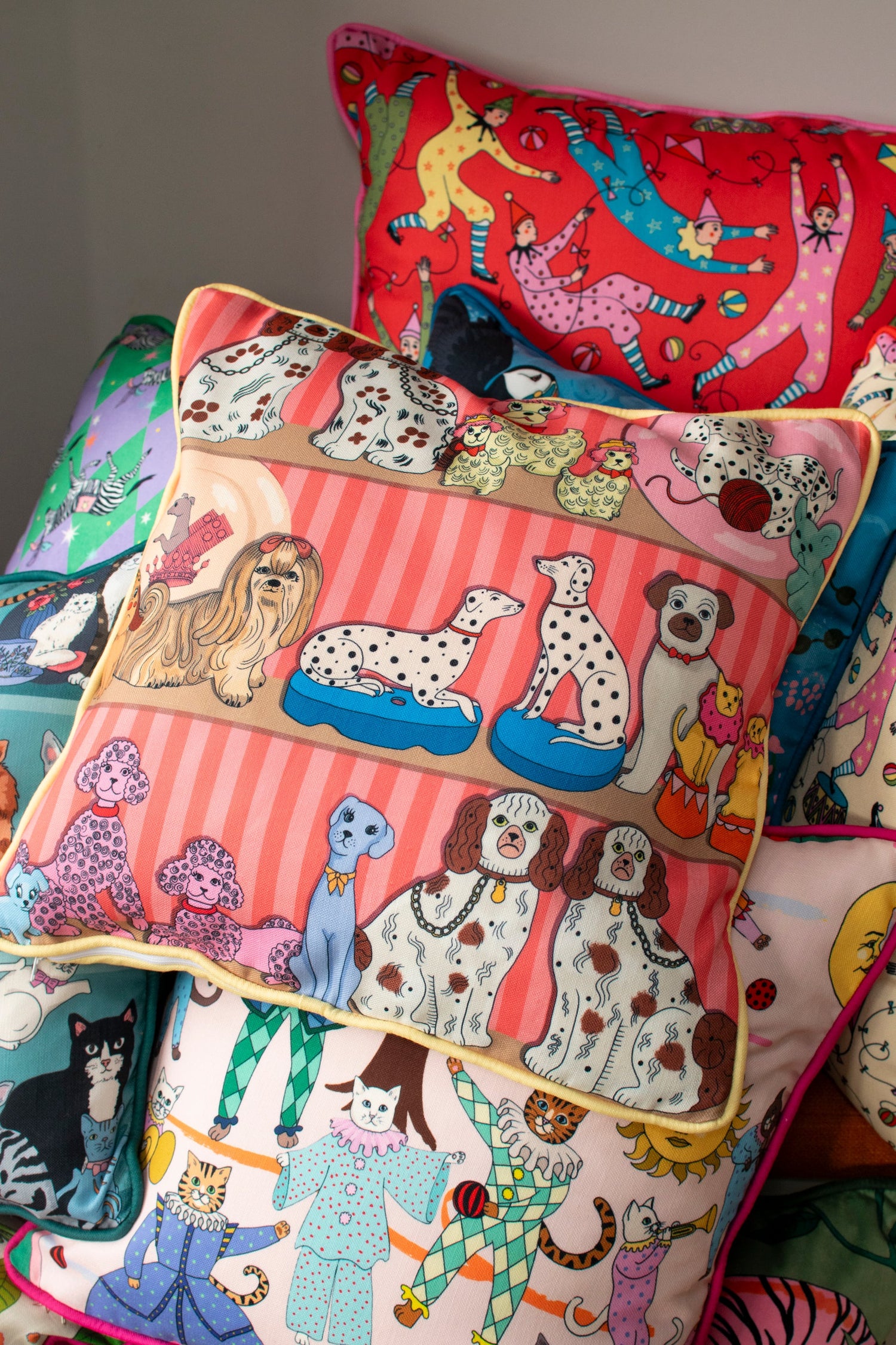 Two matching Leopard Bolster cushions on a bed with matching pink Snow Leopard cushions.Leopard Bolster Cushion, navy blue velvet with white snow leopard embroidery surrounded by leaf motifs, edged with pink contrast velvet trim. 