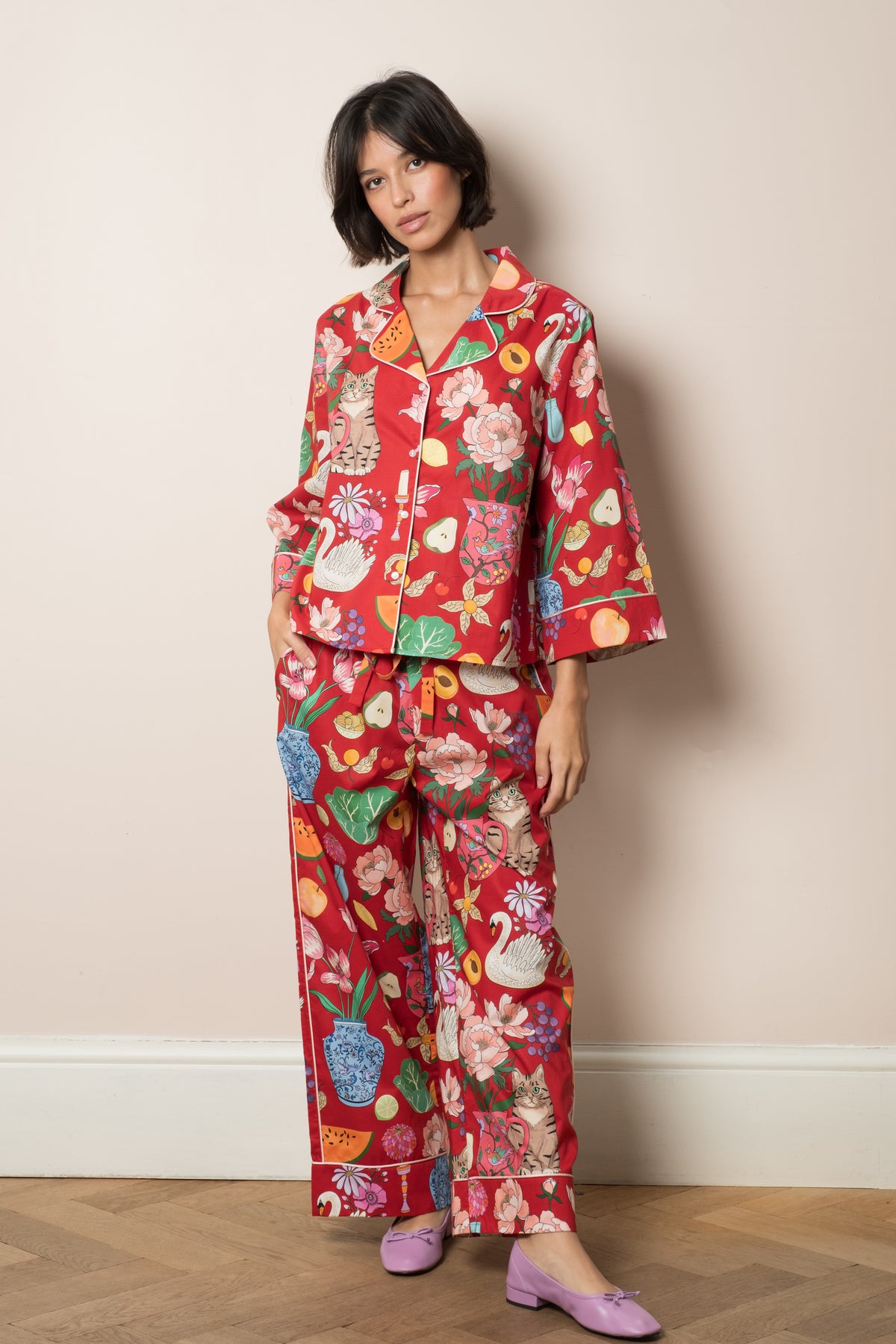 Tabletop organic cotton pyjama set in deep burgundy red, hand-illustrated still life print of swans, peonies and a cat in a jug