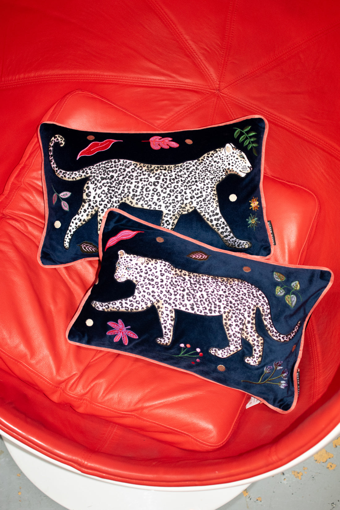 Leopard Bolster Cushion, navy blue velvet with white snow leopard embroidery surrounded by leaf motifs, edged with pink contrast velvet trim