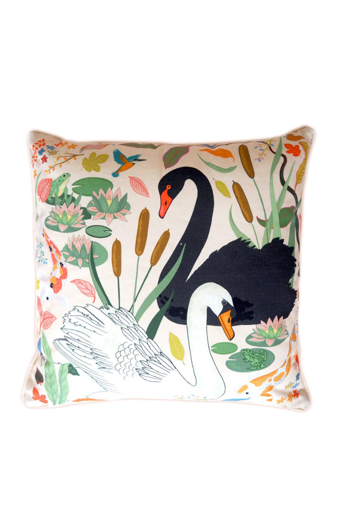 Karen Mabon Swan Lake Cushion with cream base featuring one black and one white swan, among reeds, lily pads and leaves.