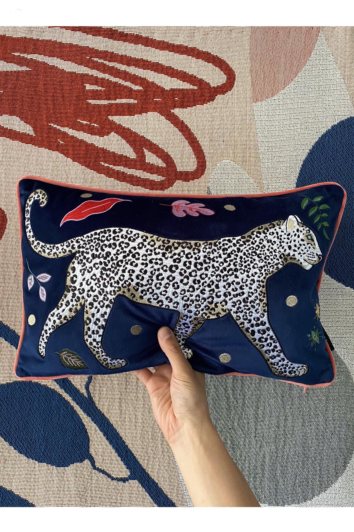 Leopard Bolster Cushion, navy blue velvet with white snow leopard embroidery surrounded by leaf motifs, edged with pink contrast velvet trim